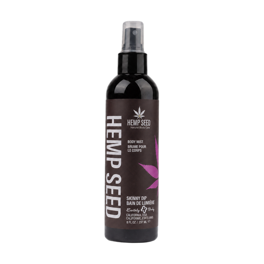 A bottle of Hemp Seed Body Mist in Skinny Dip Scent on a plain white background. The bottle is dark brown with a black spray top and features a label with white text and a pink leaf graphic.